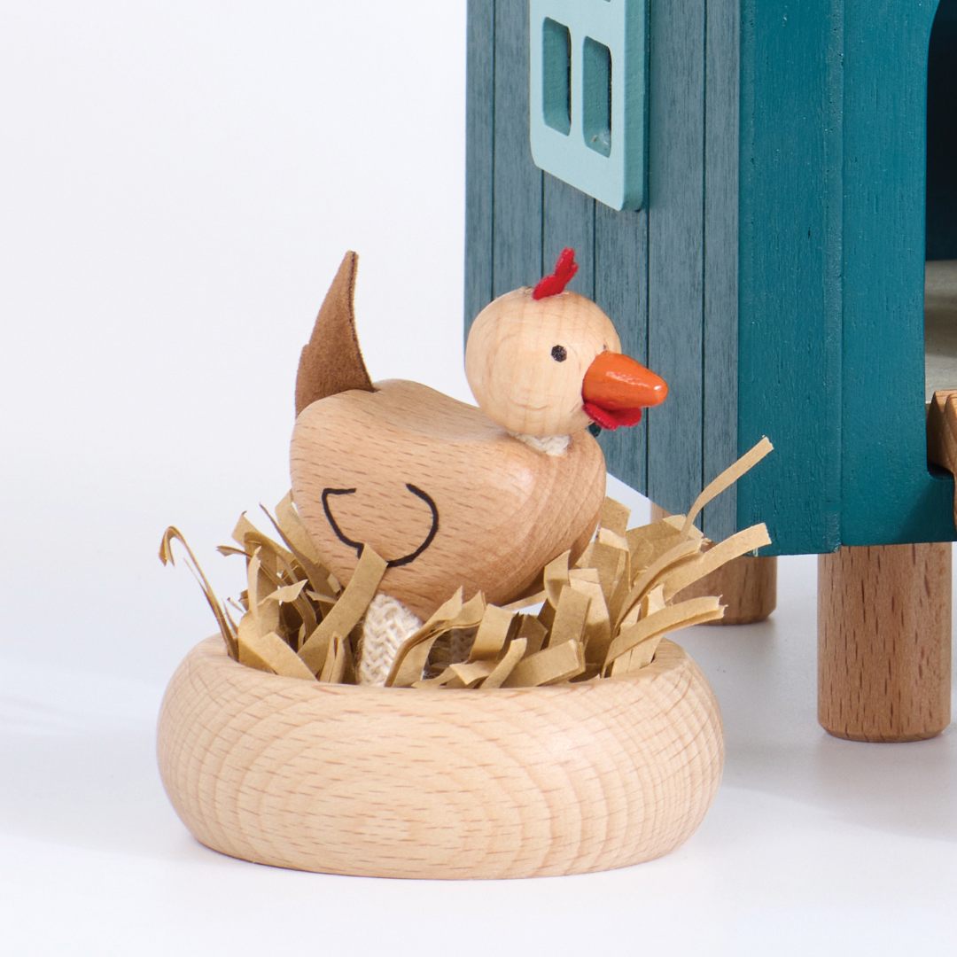 Wooden chicken with a red comb standing on a nest in front of a small wooden house.