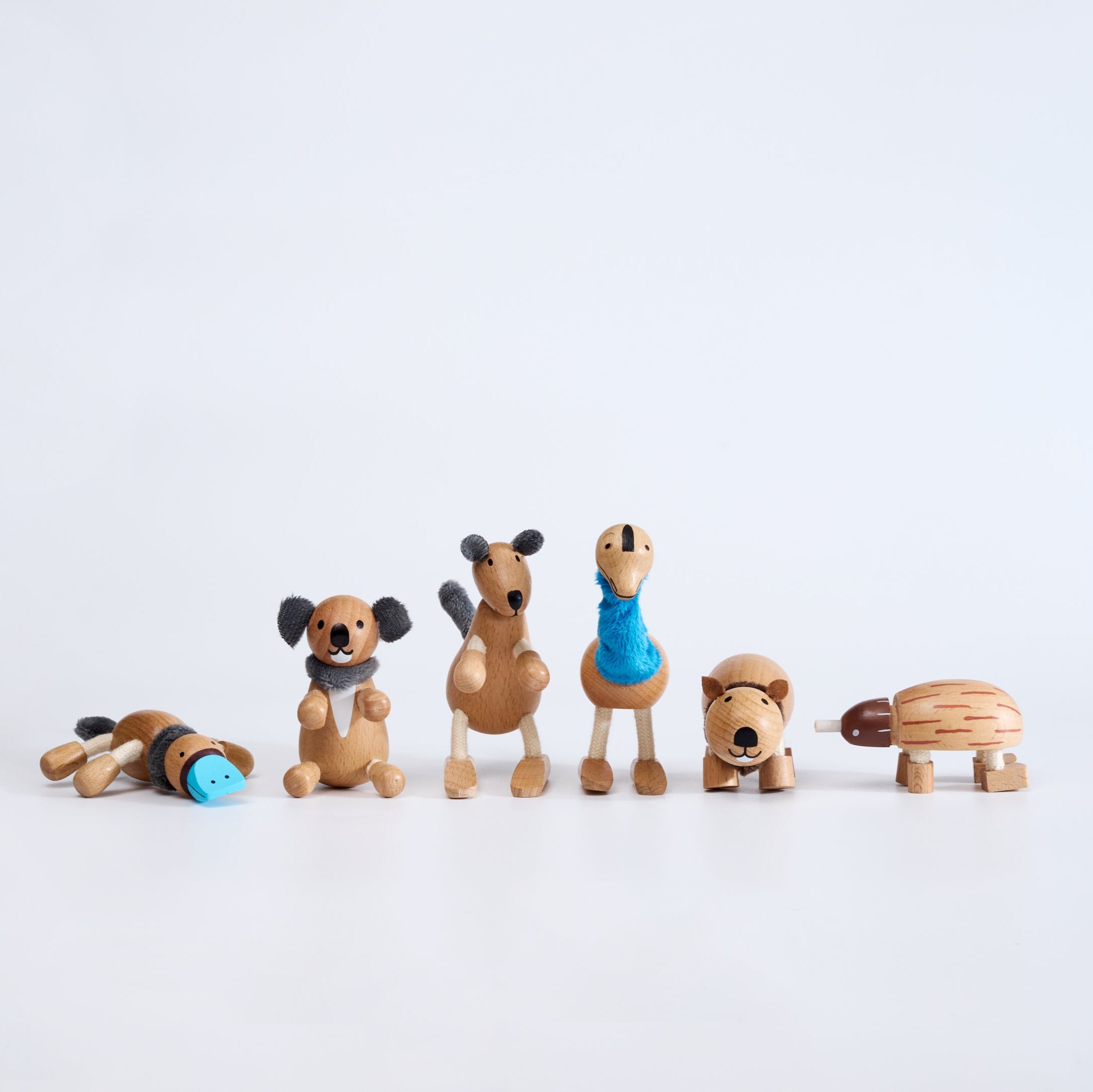 A set of six handcrafted wooden Australian animal toys, including representations of an echidna, emu, kangaroo, koala, platypus, and wombat, displayed in a line on a white background.