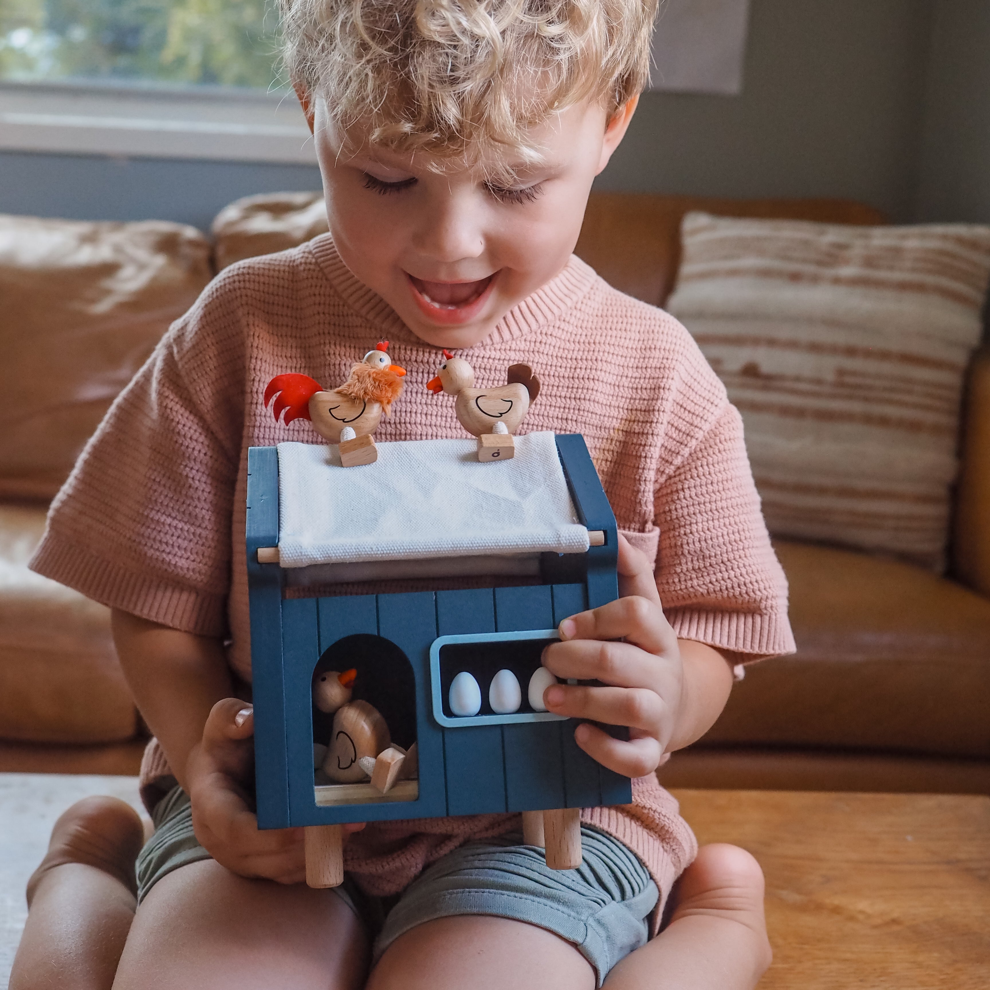 Child playing with a toy chicken coop set in a living room.