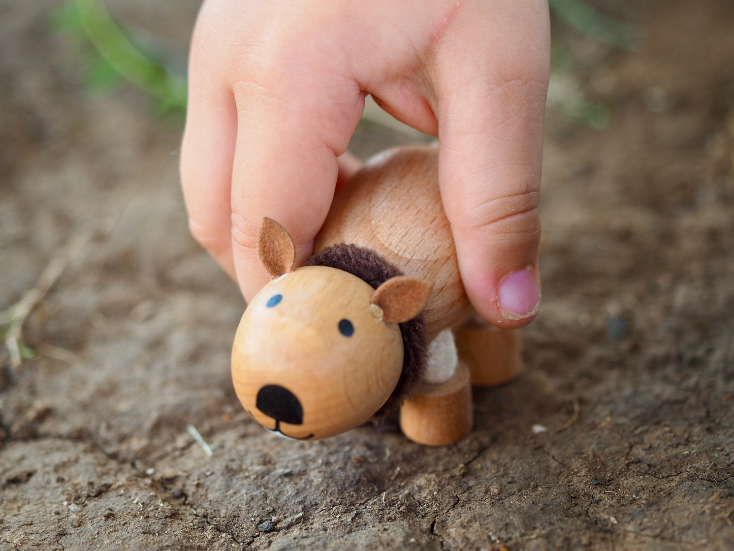 Small wooden wombat figurine held by a child's hand on dirt background