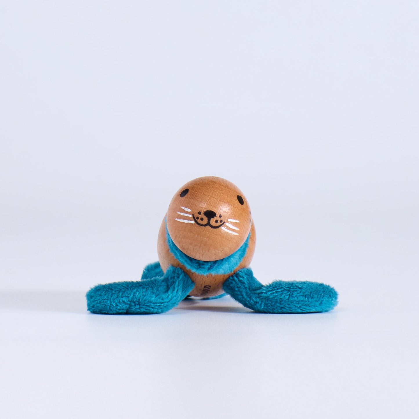 Small wooden toy seal with a face and blue string on a white background