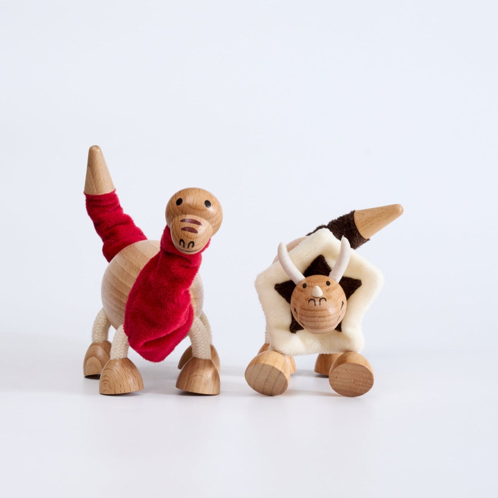 Two wooden dinosaur figures, one painted in red with a white belly, and the other in a natural wood color with a black and white pattern. Both have bendable limbs and are designed for toddlers.