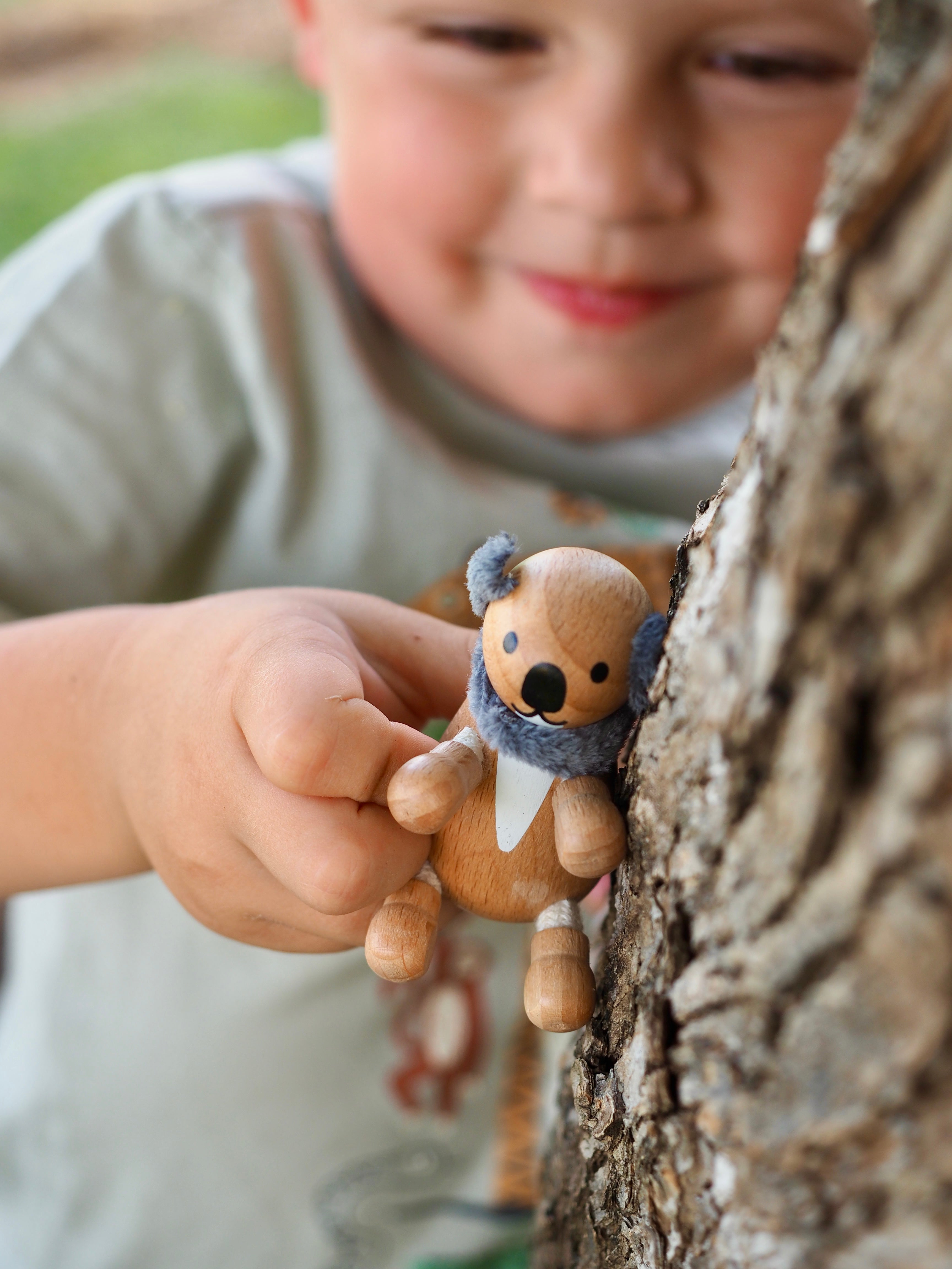 Child holding a wooden toy koala near a tree